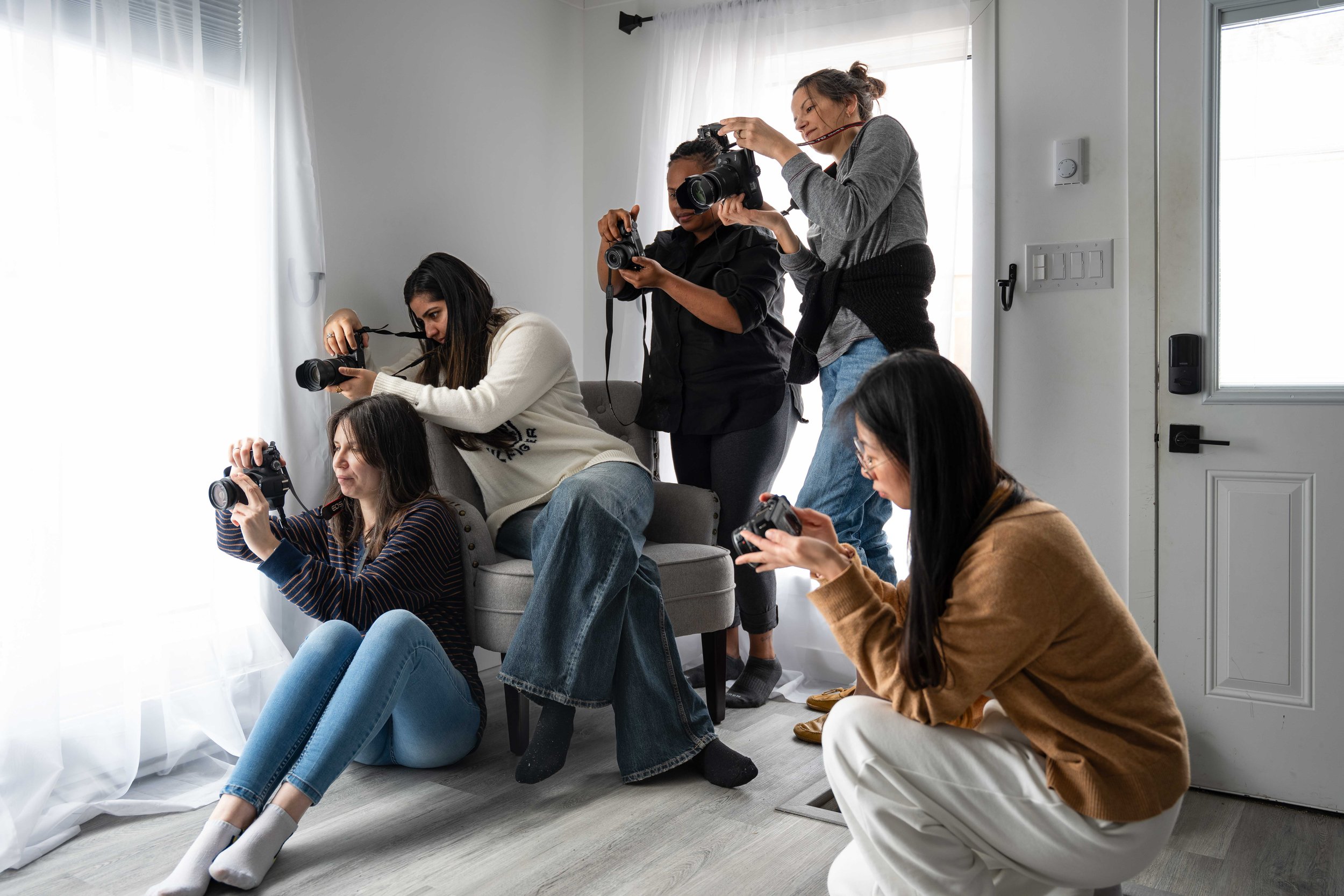 Group of photography students practicing natural light portrait photography with window light and a canvas backdrop during a hands-on digital photography course.