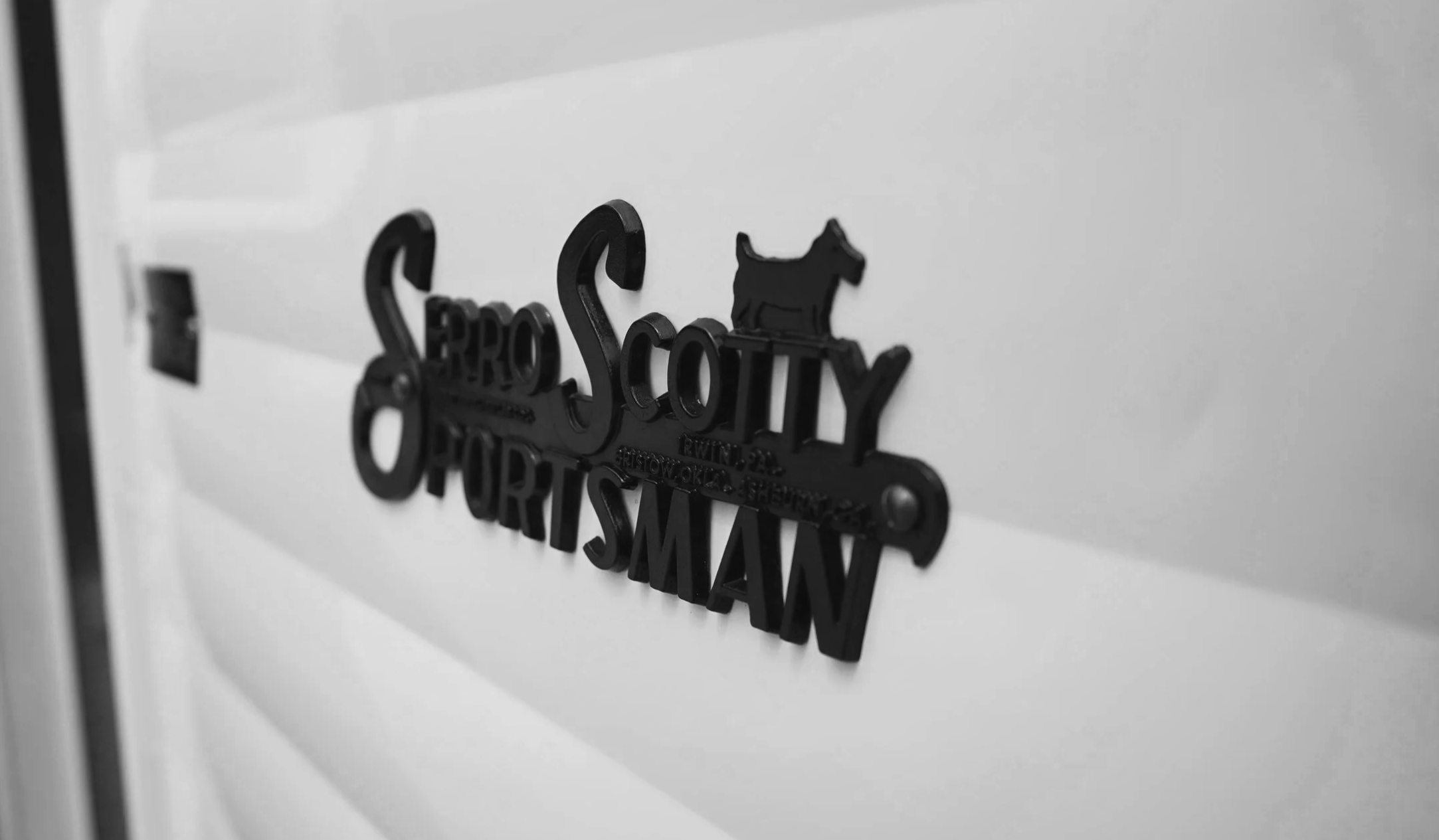 Close-up of a black metallic sign with a dog silhouette, reading "Serro Scotty" on a white surface.