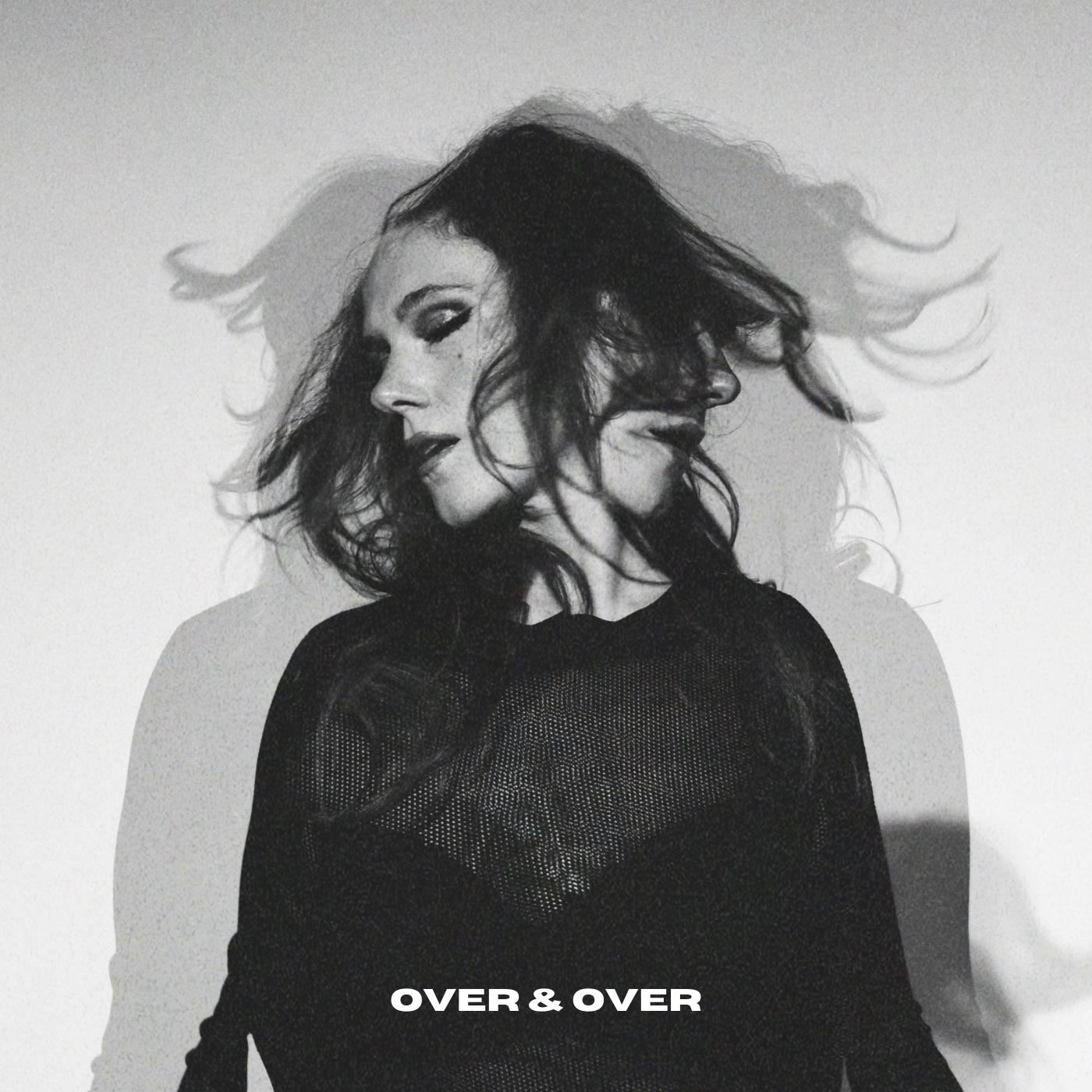 Black and white photo of Suzanne Sheer with wavy hair, looking to the side with a serious expression, wearing a dark mesh top, with the words 'OVER & OVER' written at the bottom.