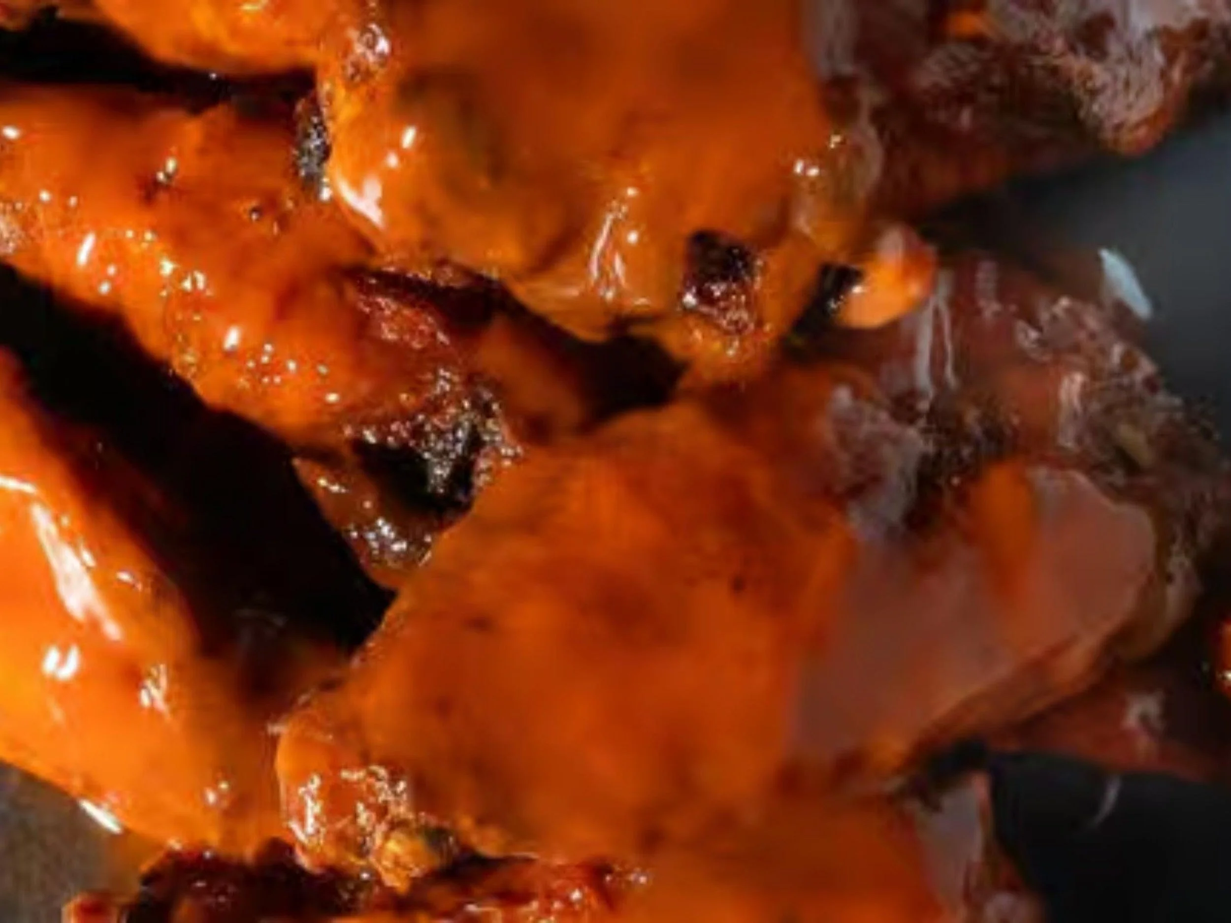 Close-up of a piece of grilled chicken with orange barbecue sauce.