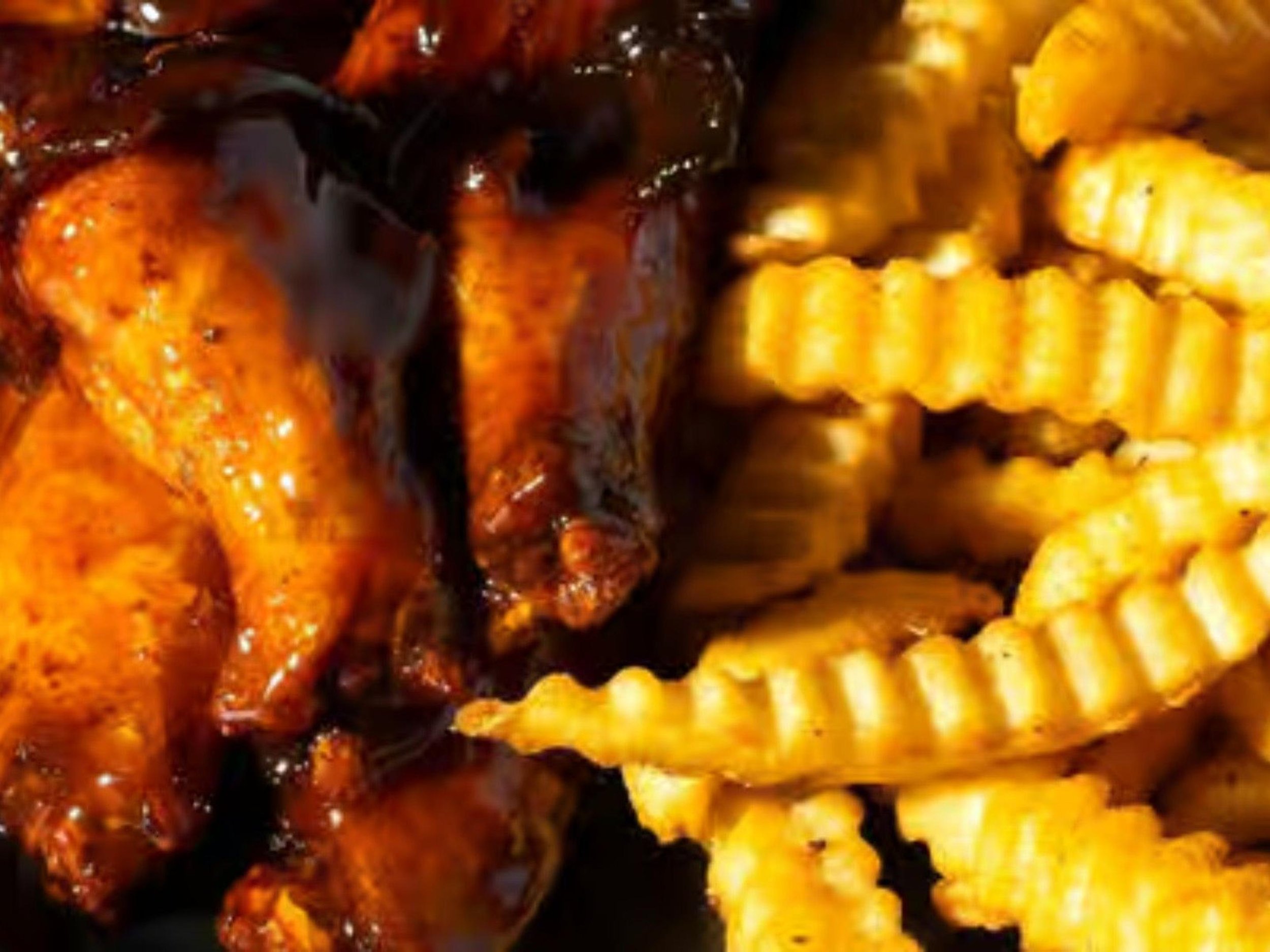 Close-up of grilled chicken with golden crispy skin and crisscrossed waffle-cut fries.