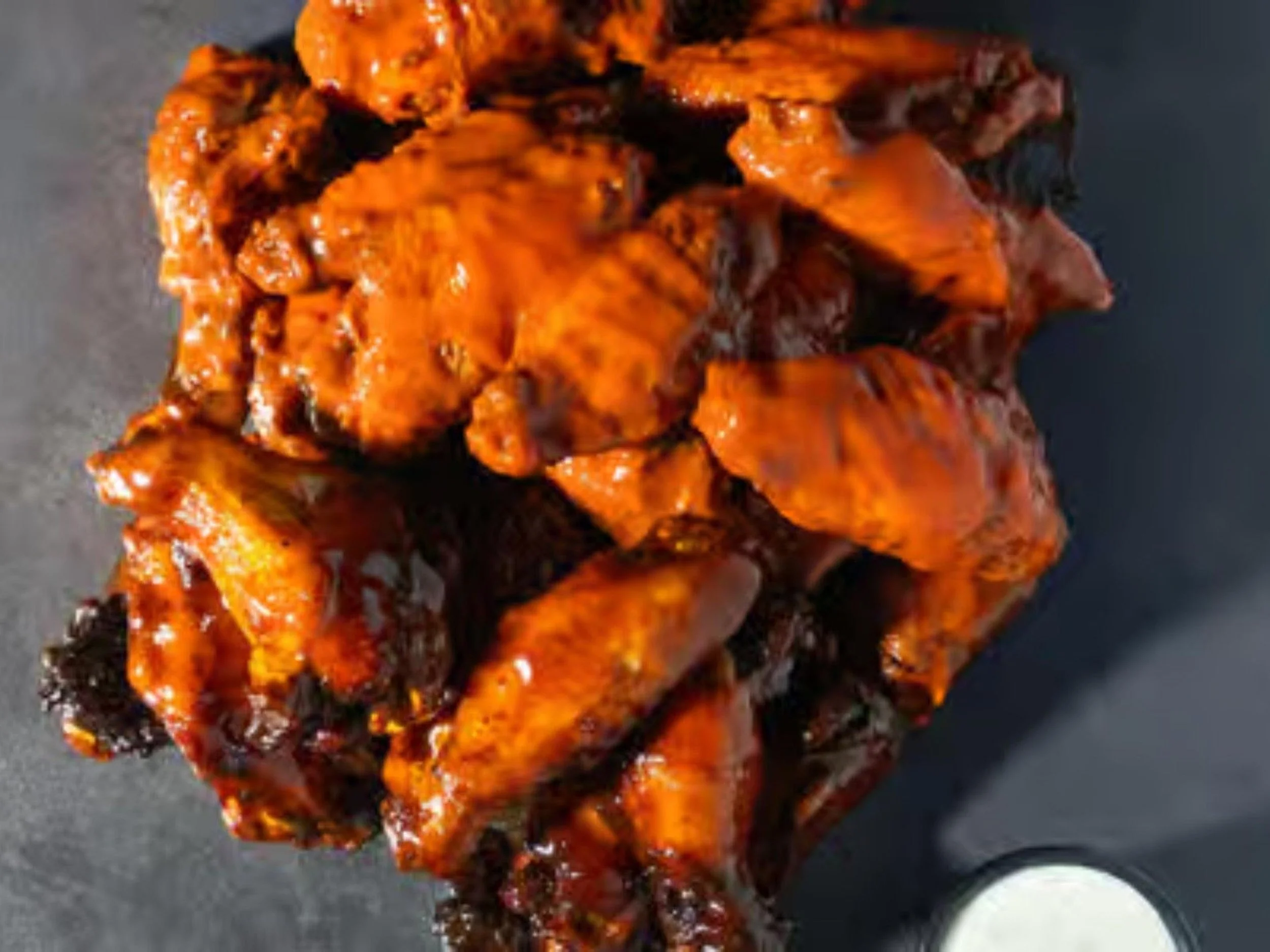 Close-up of grilled or roasted meat covered in barbecue sauce on a dark surface.