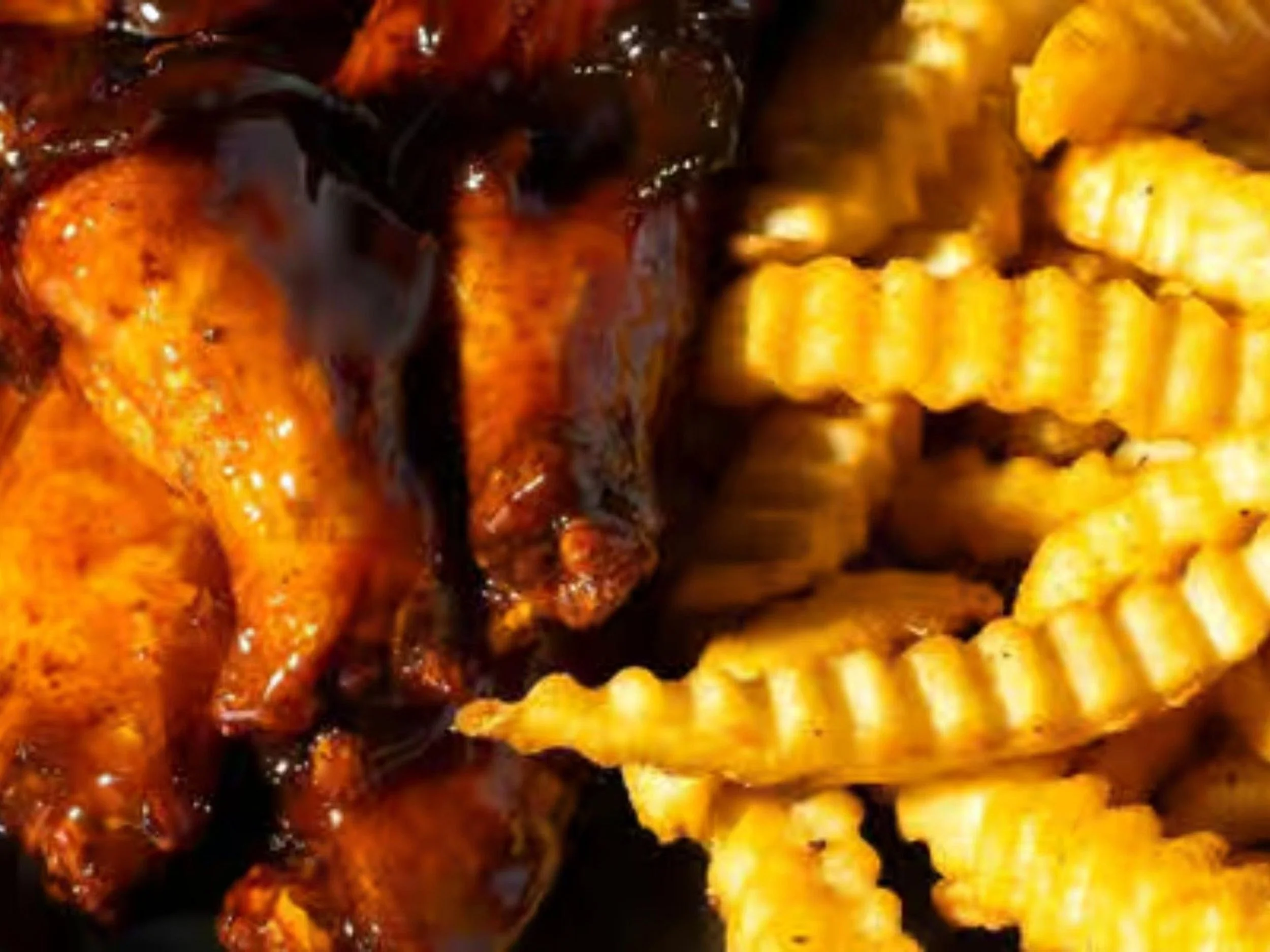 Close-up of roasted chicken with crispy, glazed skin next to crinkle-cut French fries.