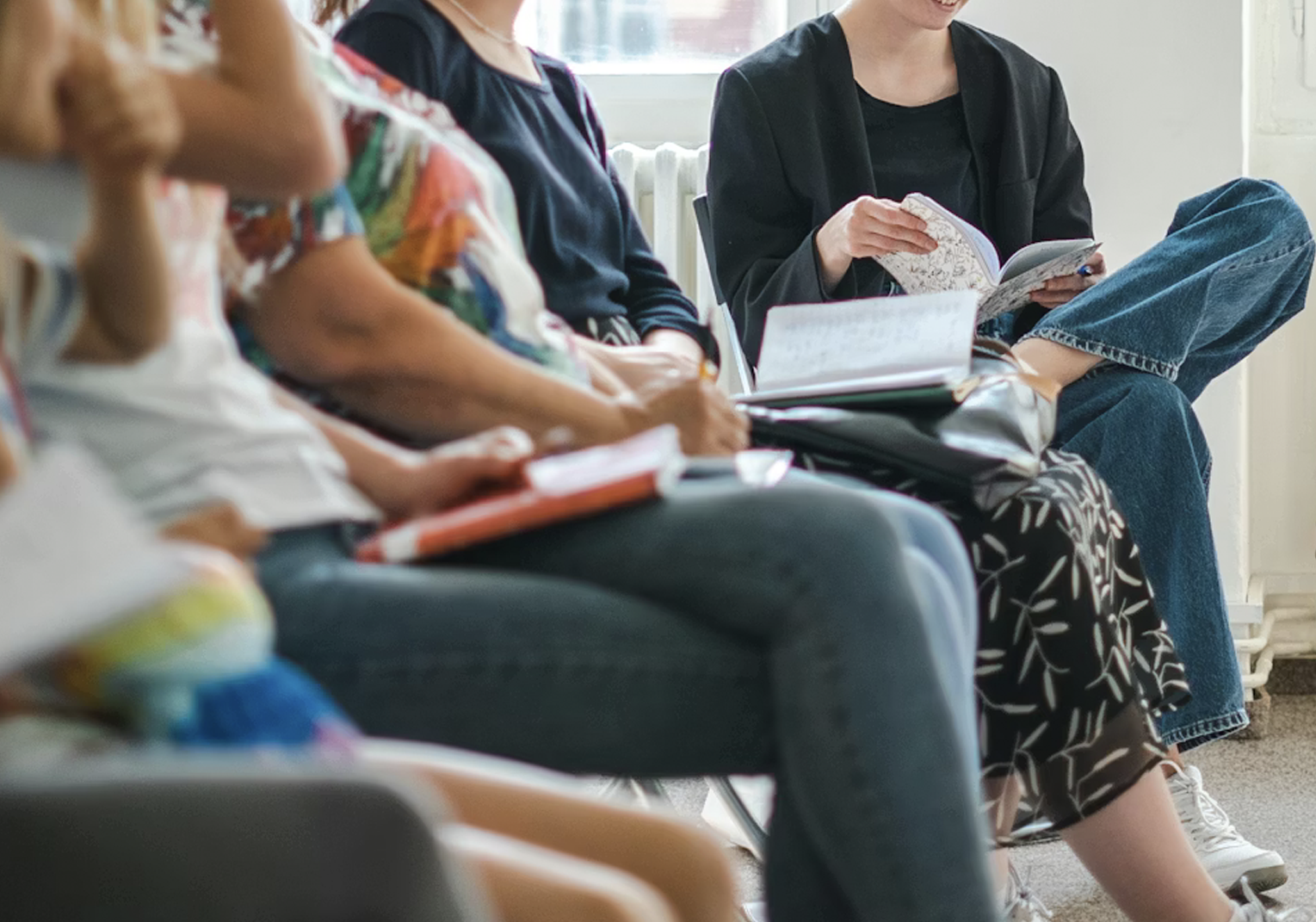 People seated on chairs reading books or notebooks, possibly in a waiting area or classroom.