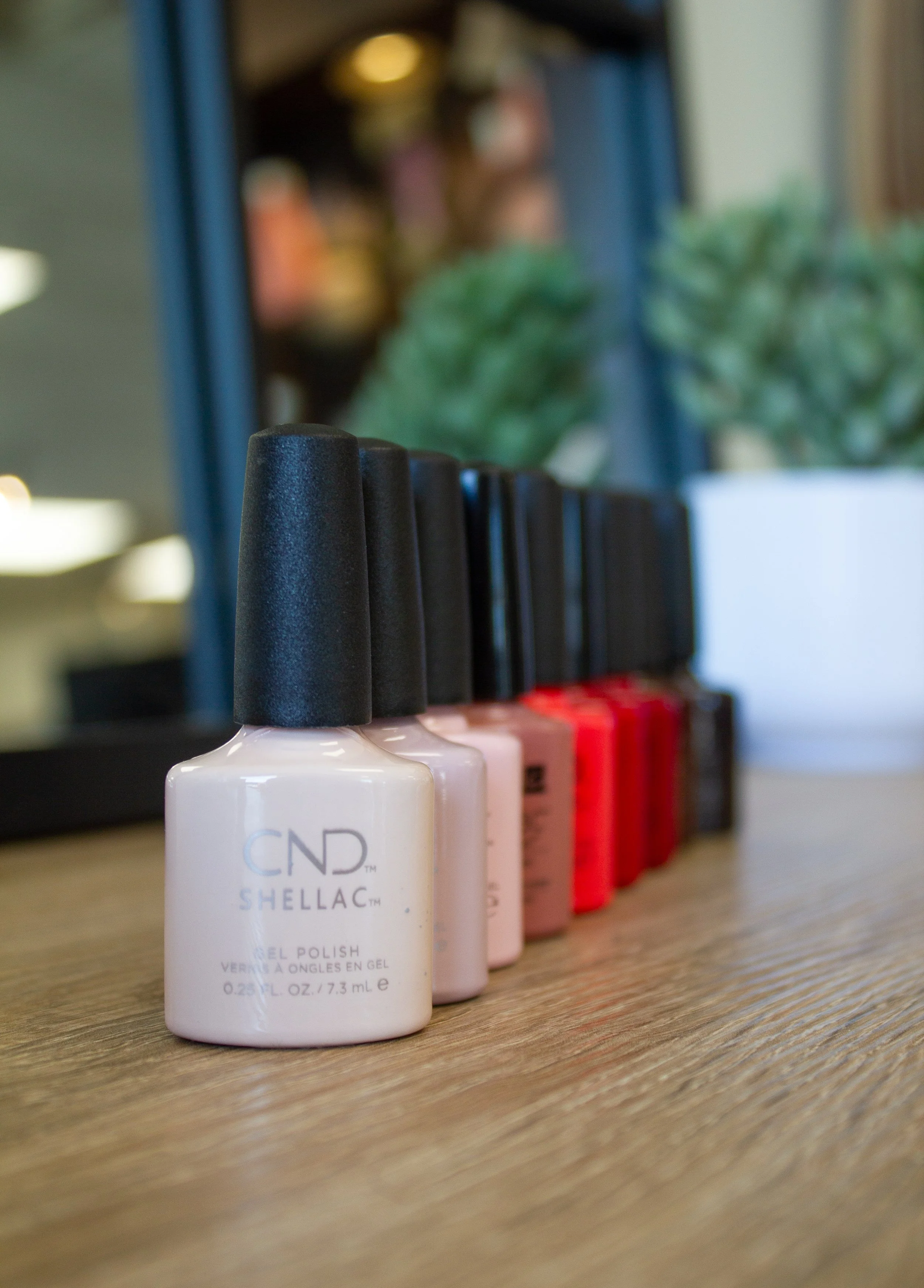 Close-up of various bottles of nail polish on a wooden surface, with the front bottle labeled 'CND Shellac.'