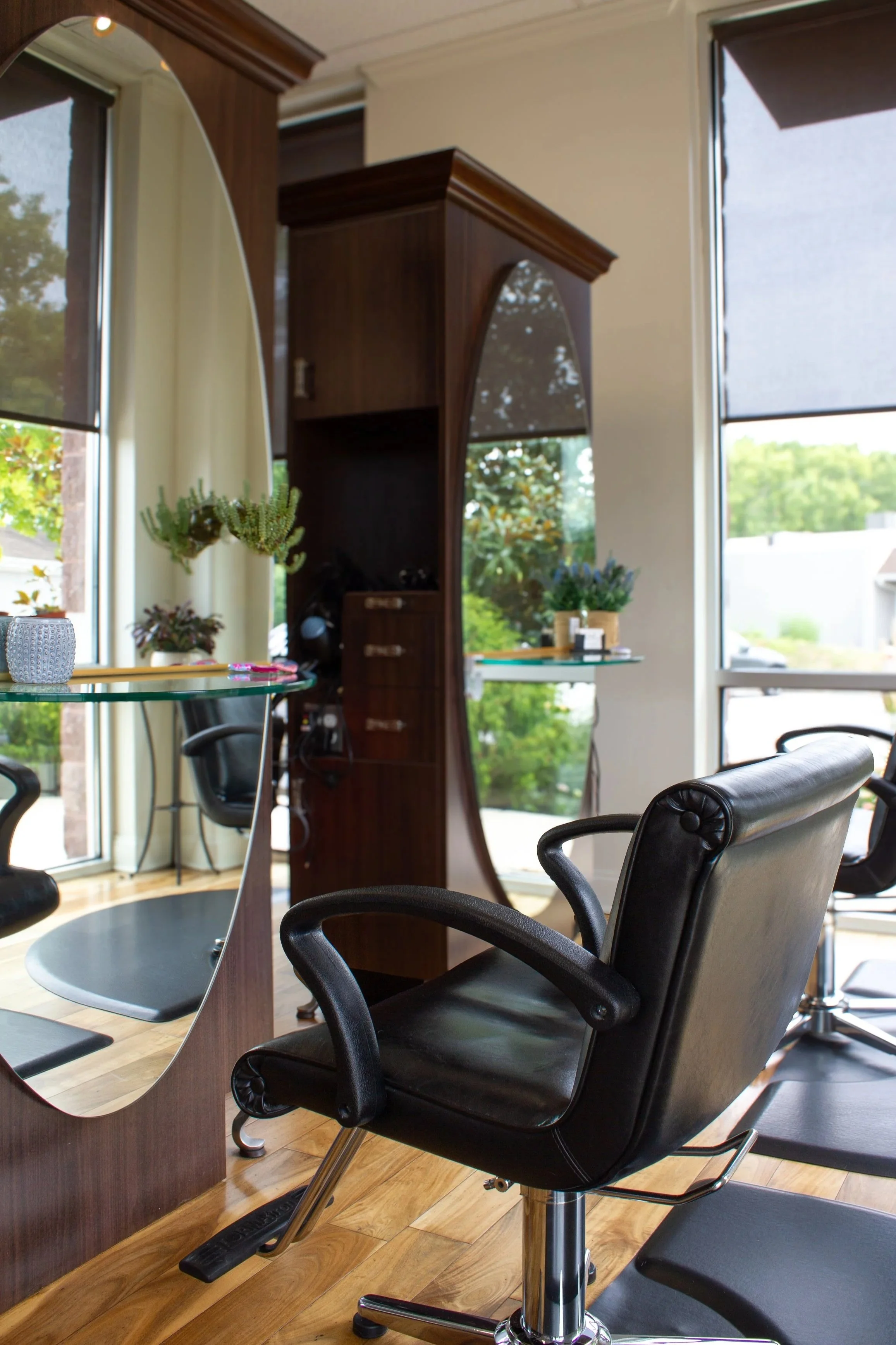 Prestige Salon chair in front of a large window with shades, with plants on a shelf behind. Reflection of the window seen in a mirror.