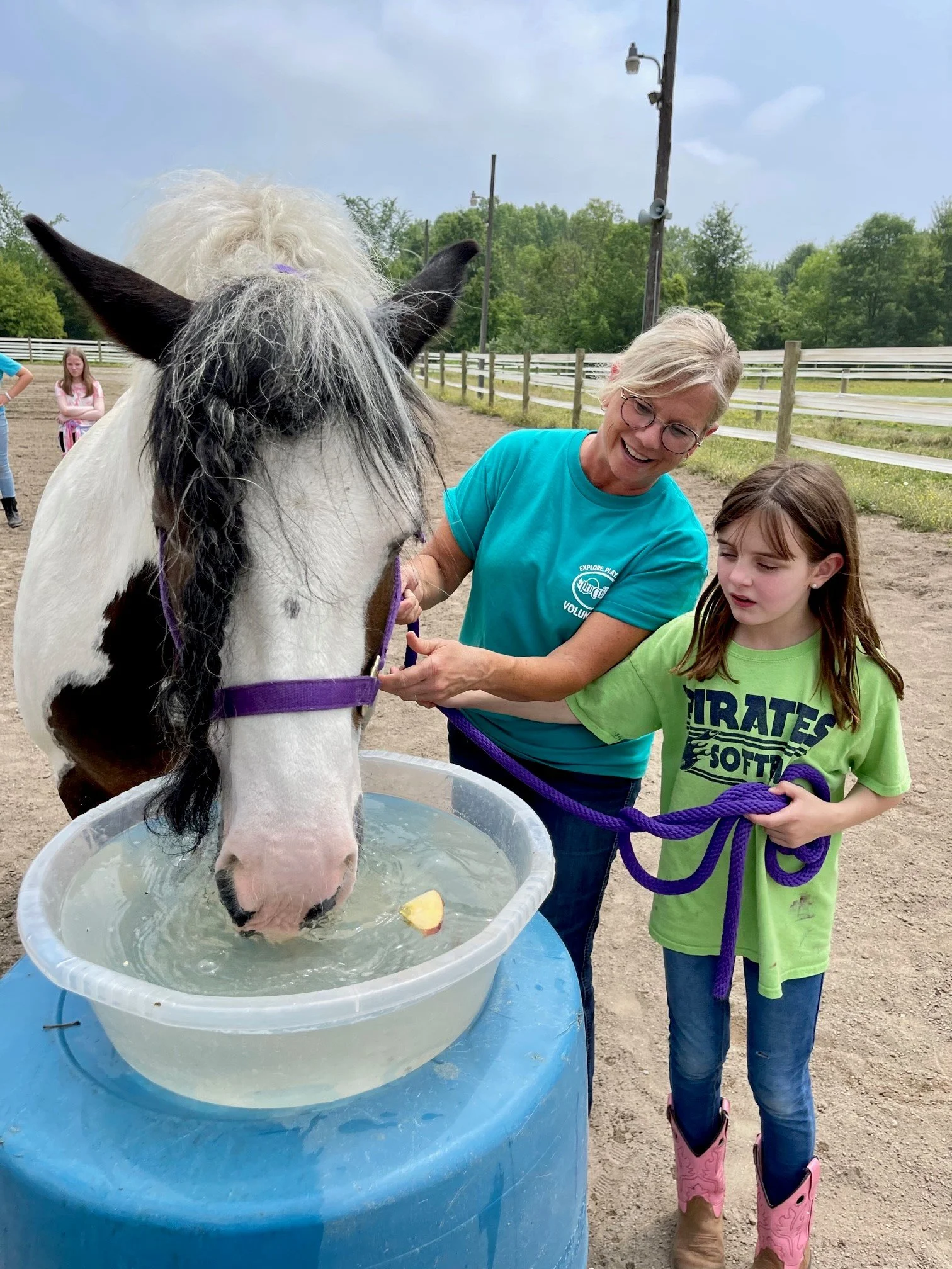 A horse at Camp Red Cedar is being watered while a staffer and young camper watch.