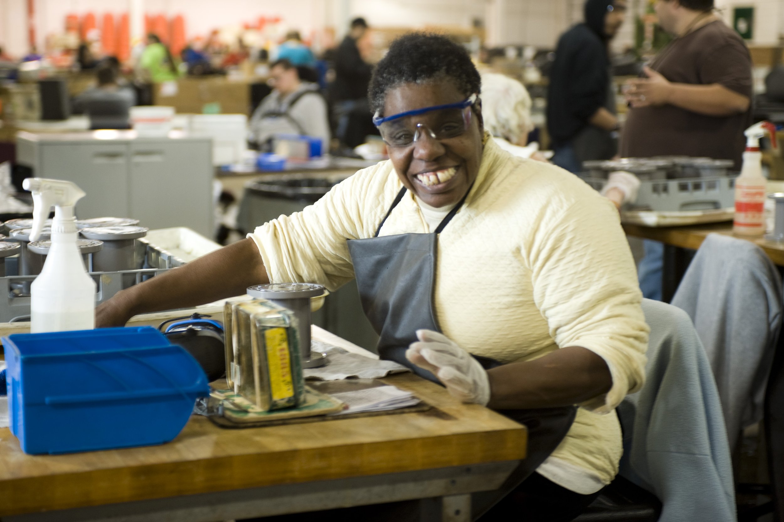 Image of an AWRC Industries worker in a manufacturing or workshop environment with other people in the background.