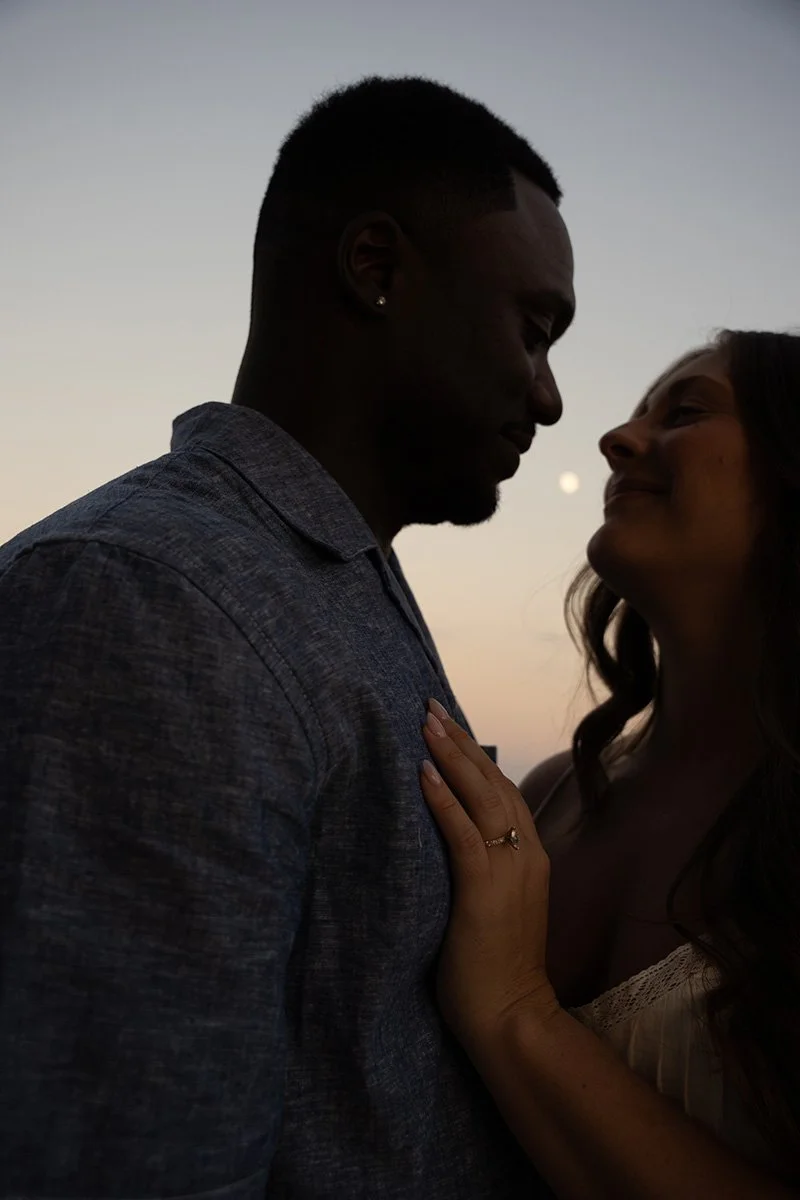 A silhouette of a couple close together during sunset, with their faces nearly touching, expressing intimacy.