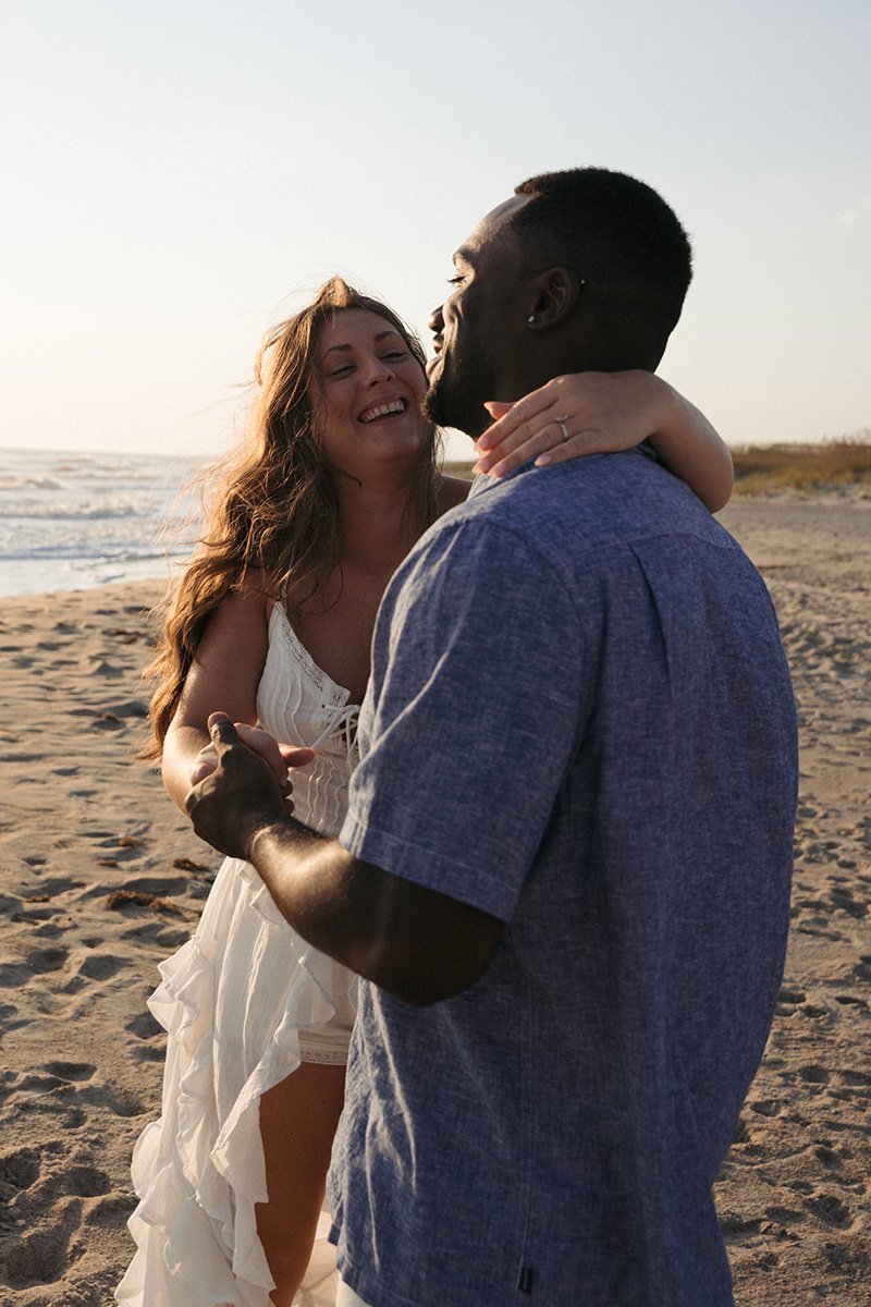 A couple dancing and embracing on the beach during sunset, smiling and enjoying each other's company.
