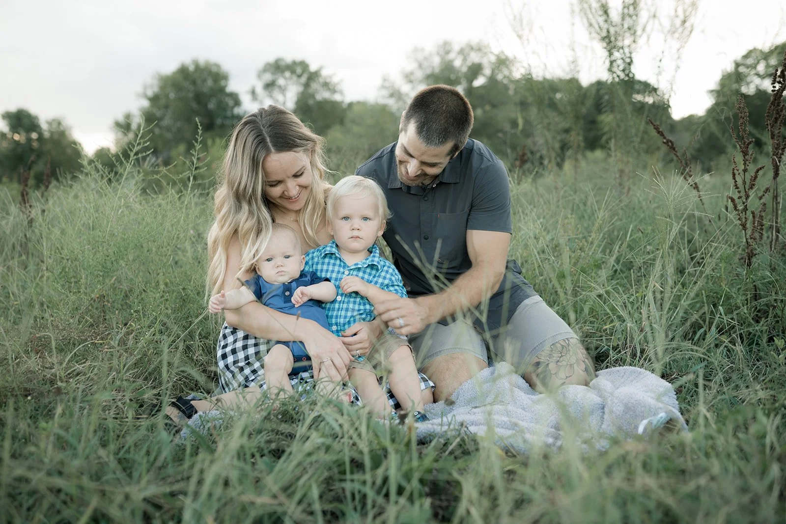 This is an image of a family photo shoot at Chantilly Park in Charlotte, North Carolina. There is a father and mother and two small children. They are wearing checkered shirts and sitting in the grass together.