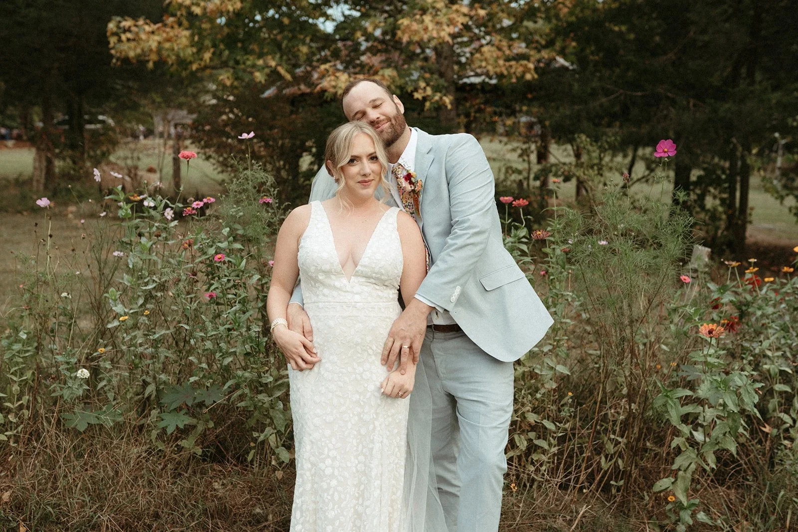This is an image of a wedding couple standing in front of a  row of wildflowers on the Shakori Hills festival grounds in North Carolina.