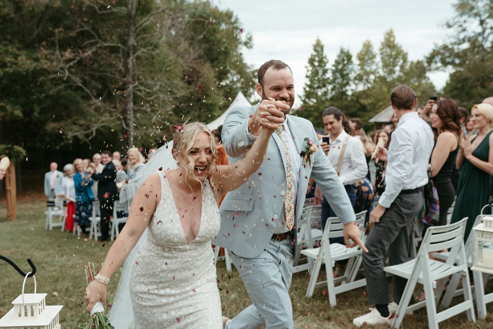 This is an image of a couple walking down the aisle of their intimate wedding at the Shakori Hills Music Festival Grounds. They are holding hands high and smiling.