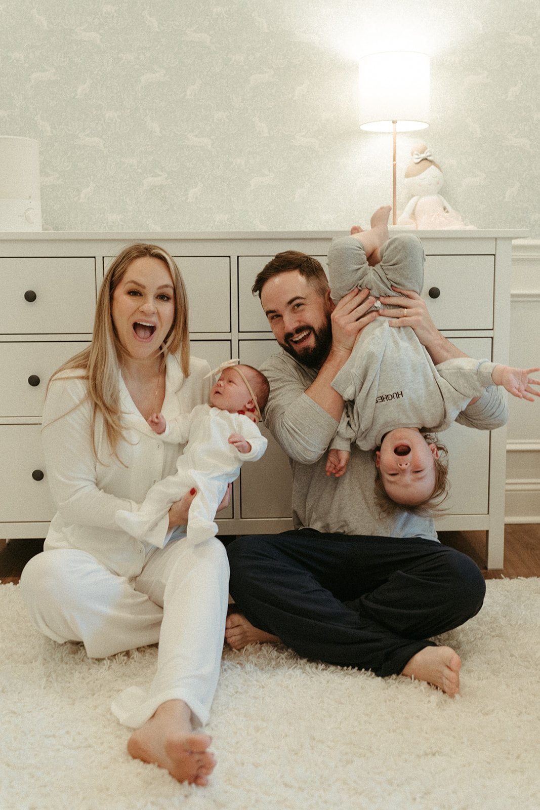 A family sits in pajamas at home on the floor, smiling at the camera in a silly pose for an at home photo session.