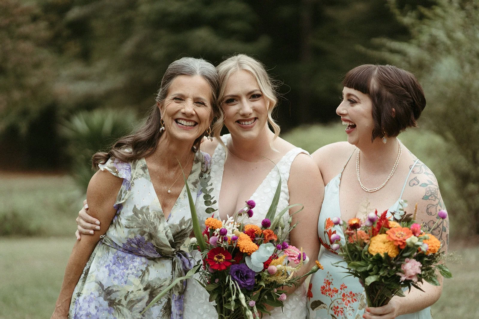 Three women are standing embracing and smiling after seeing their friend in her wedding dress for a first look.