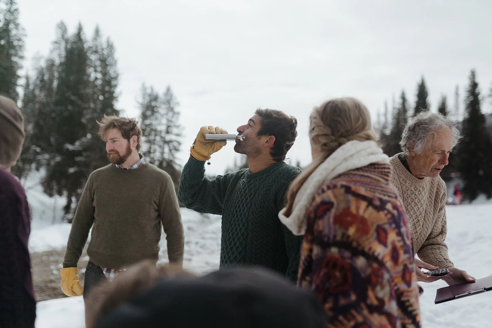 A group of people standing in the snow during a couple's winter elopement toast with a flask of whiskey.