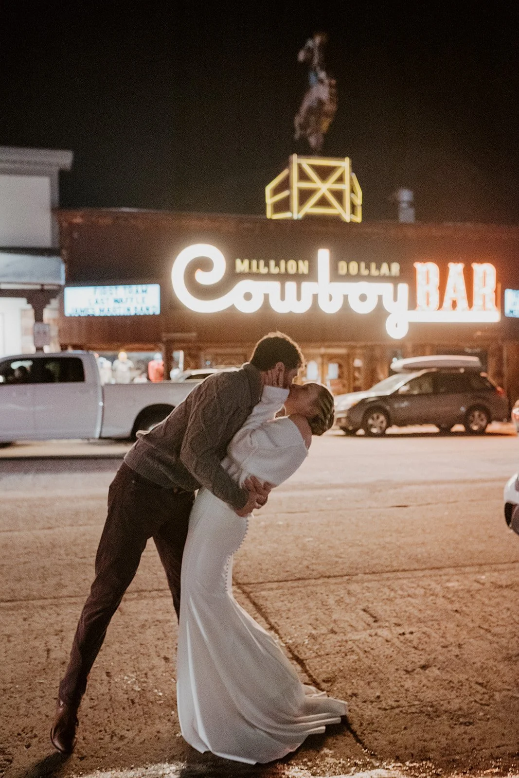 A husband and wife pose kissing outside the Cowboy Bar in Jackson Hole on their wintery wedding day