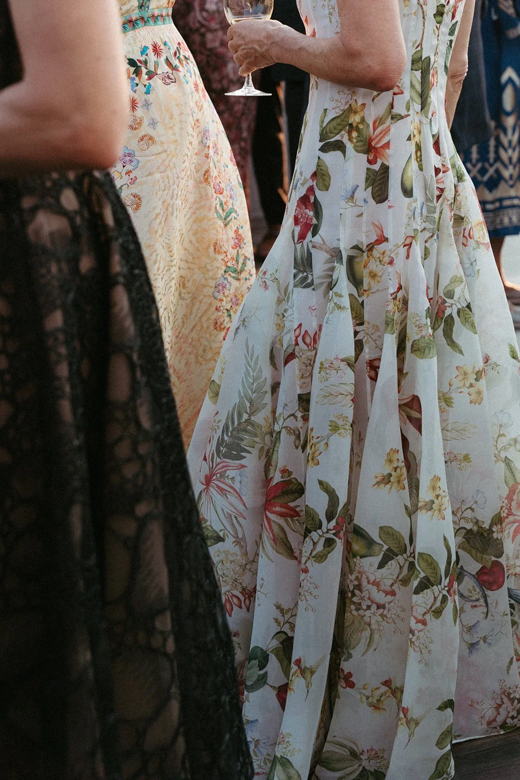 Close-up view of women wearing colorful floral dresses at a social gathering, with one woman holding a wine glass.
