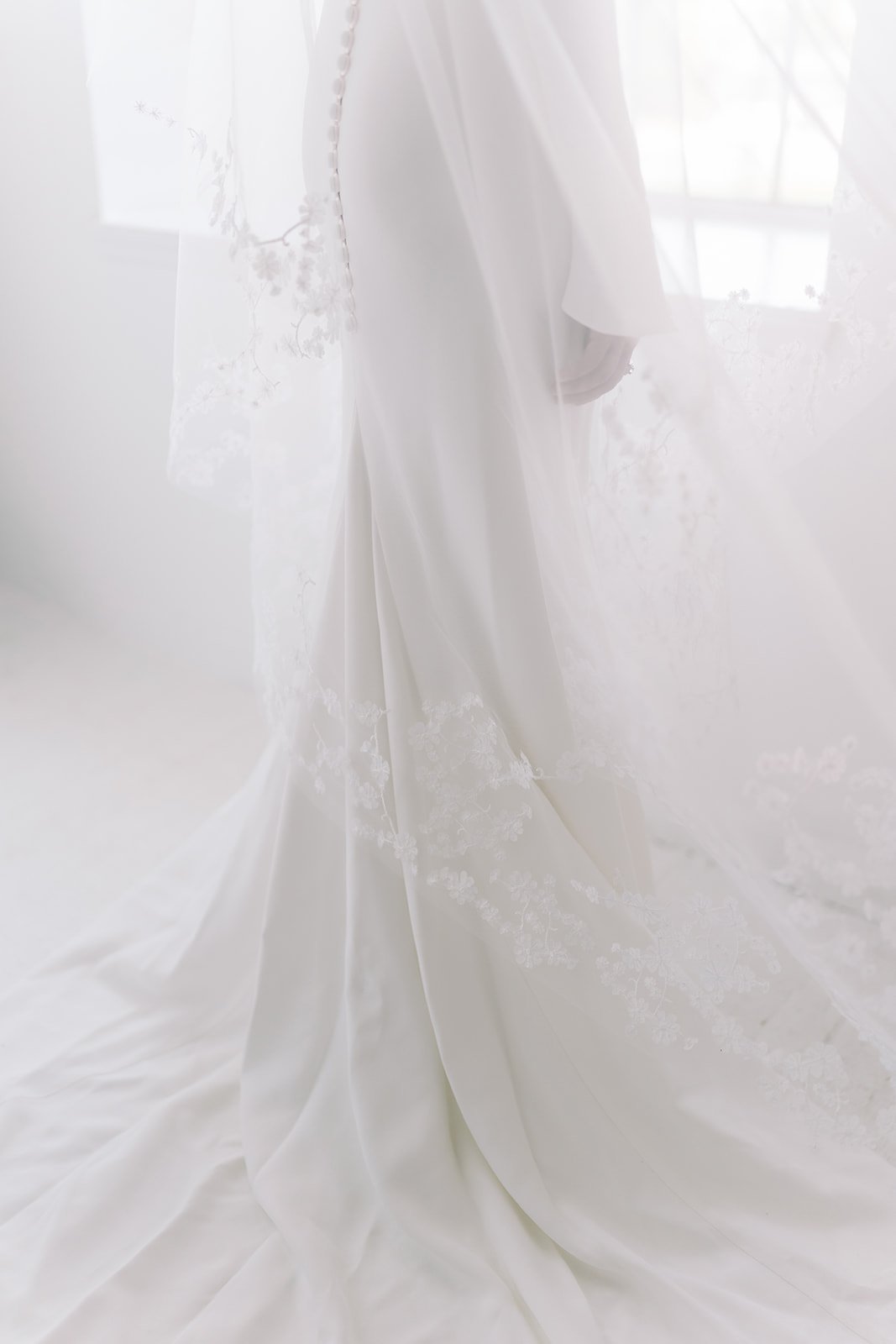 A person in a white wedding dress standing near a window with light coming through, soft focus and a dreamy, ethereal atmosphere.
