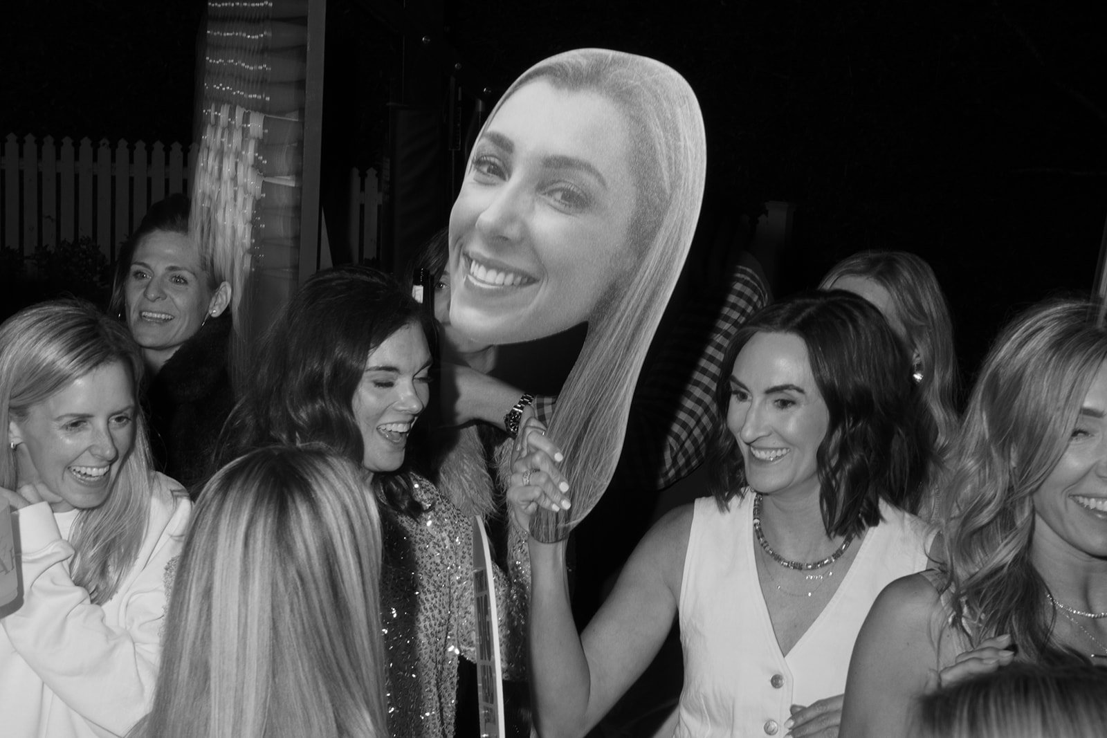 Group of women at a celebration with a large cardboard cutout of a smiling woman's face.