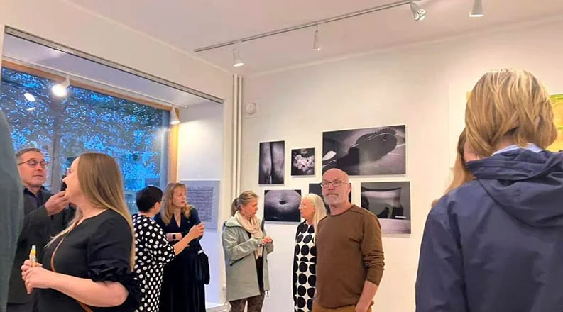 People attending an art gallery exhibit, standing and conversing, with black and white photographs displayed on the wall.Life Sentence opening exhibition in Helsinki, Finland.