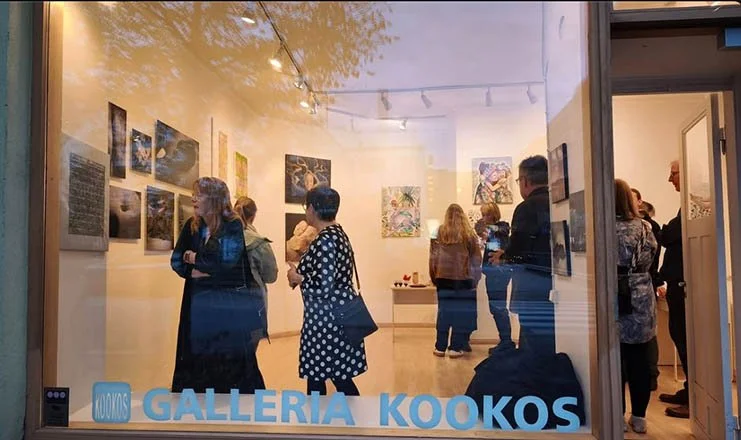 View of an art gallery with visitors viewing paintings on the walls, seen through a window with a sign reading 'GALLERIA KOO KOS' at the bottom.Life Sentence opening exhibition in Helsinki, Finland.