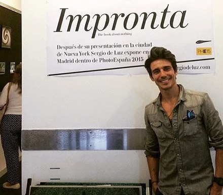 former NYCB principal dancer miling standing next to a large sign that says 'Impronta'. The sign has additional text in Spanish about a book presentation by Sergio de Luz in Madrid during PhotoEspaña 2015.Mad is Mad gallery.