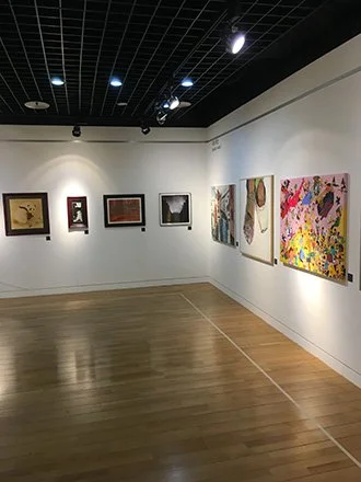 Art gallery with framed paintings and colorful abstract artwork on white walls, wooden floor, and ceiling lights.exhibited in Seoul Korea.