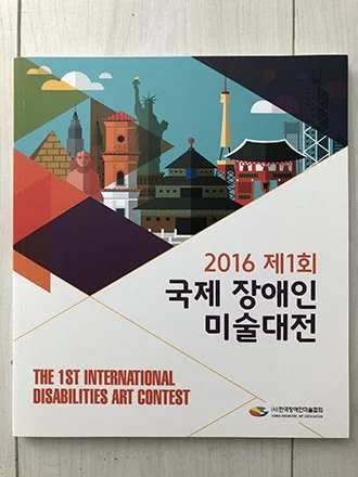 Cover of a booklet for the 1st International Disabilities Art Contest in 2016, featuring stylized illustrations of various landmarks and buildings. exhibited in Seoul Korea.