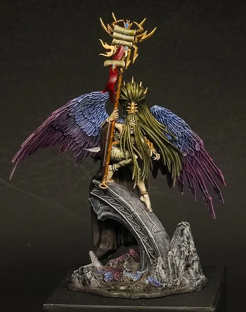A detailed fantasy sculpture of a mythical creature with large, colorful wings, a lumbering body, and a crown-like headpiece, perched on a rocky base.