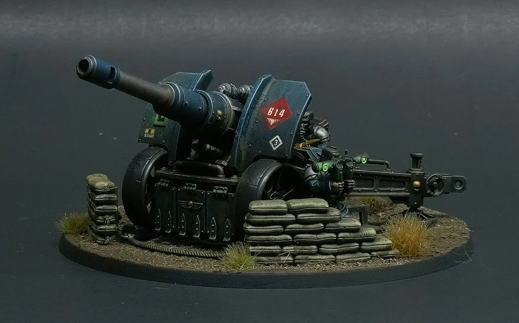 Miniature model of a military artillery gun with sandbags, grass, and a soldier figure operating the weapon.