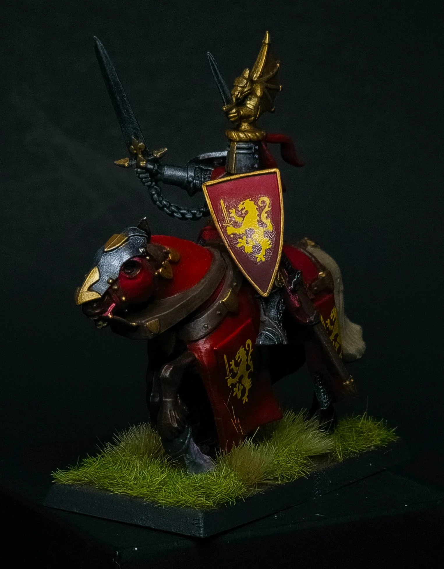 Miniature medieval knight figurine riding a horse with armor and a shield, placed on a grassy base against a black background.