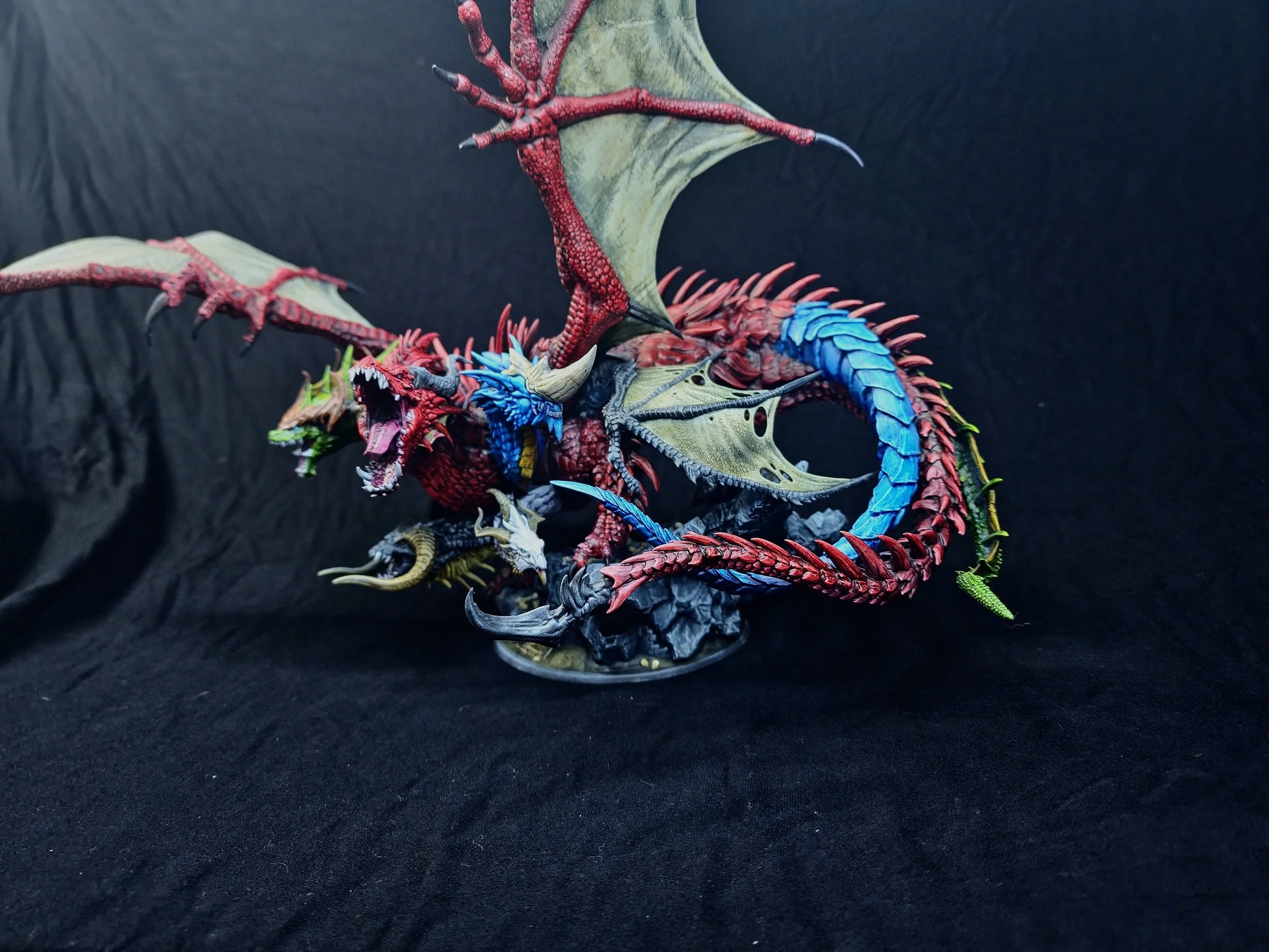 Close-up of a colorful dragon figurine with detailed scales, wings, and claws, set against a dark background.