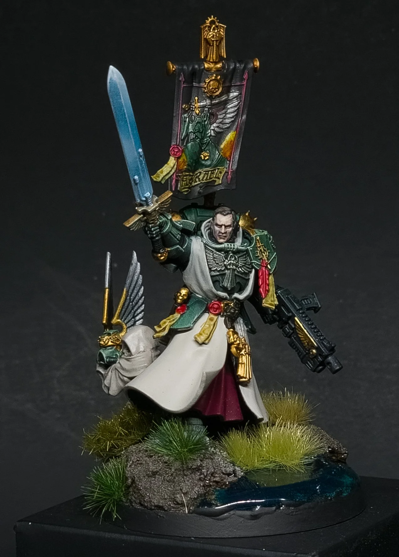 A detailed painted miniature figurine of a futuristic warrior in armor holding a sword aloft and a gun in the other hand, standing on a scenic base with greenery and water.