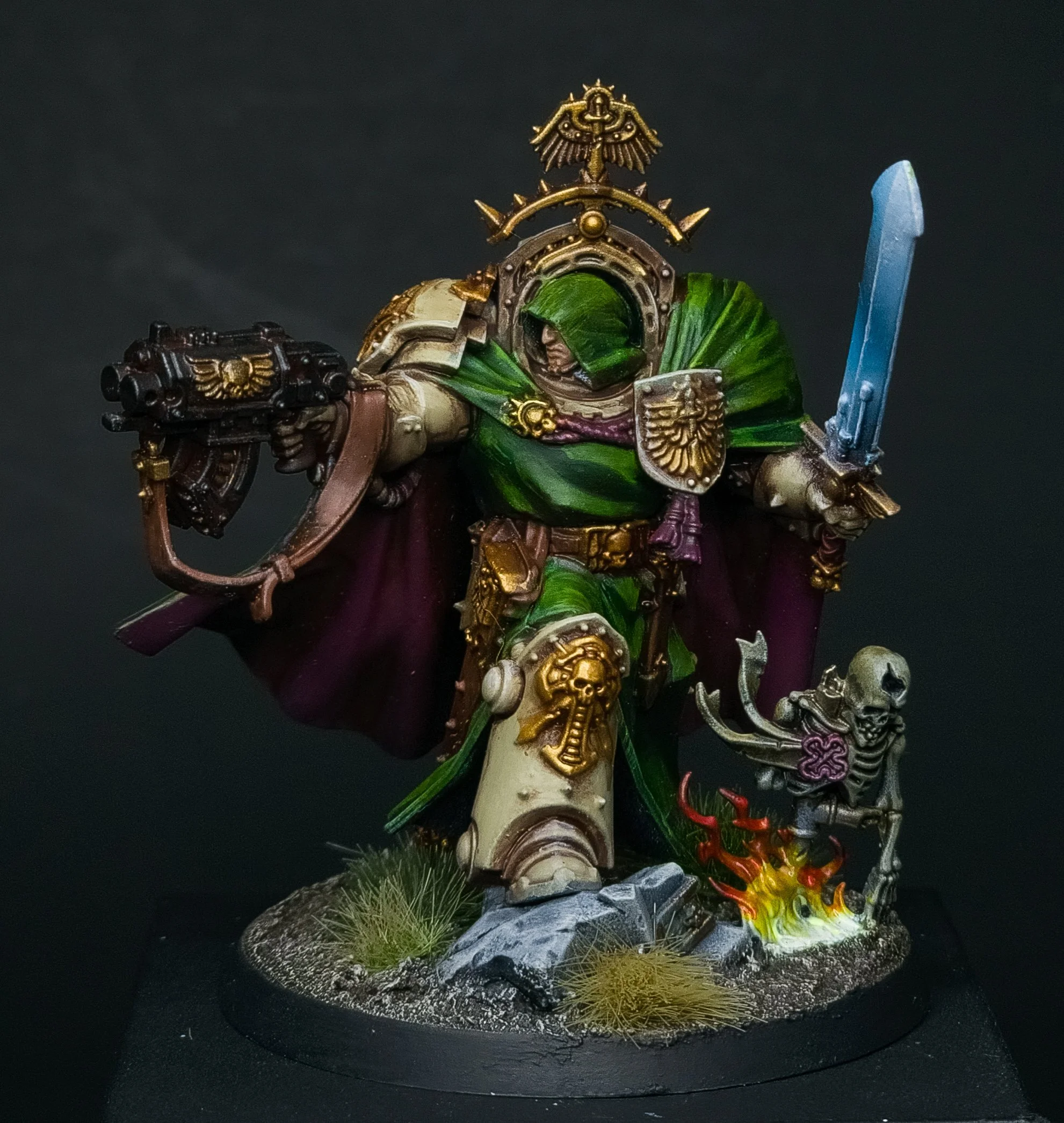 Miniature figure of a fantasy warrior, wearing armor with gold accents, holding a sword and gun, standing on a decorated base with rocky terrain, grass, and flames.