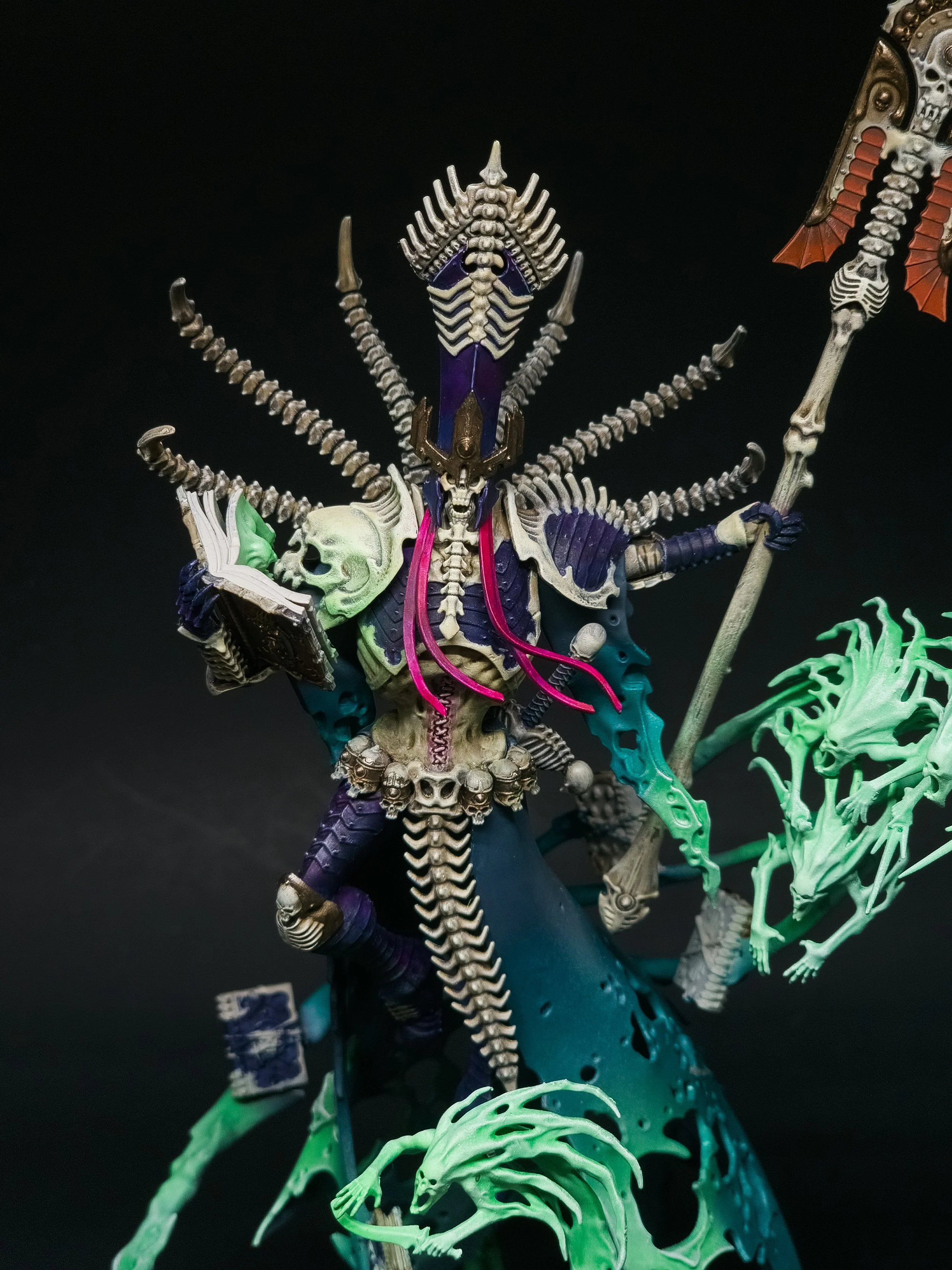 A detailed figurine of a skeletal demon with multiple skulls and bones, holding a staff, surrounded by green energy effects.