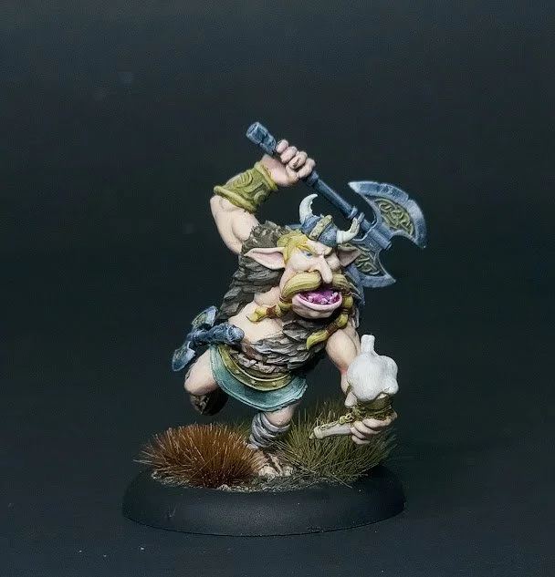 Miniature fantasy dwarf warrior figurine with an axe, holding a shield, and standing on a detailed base with grass and rocks.