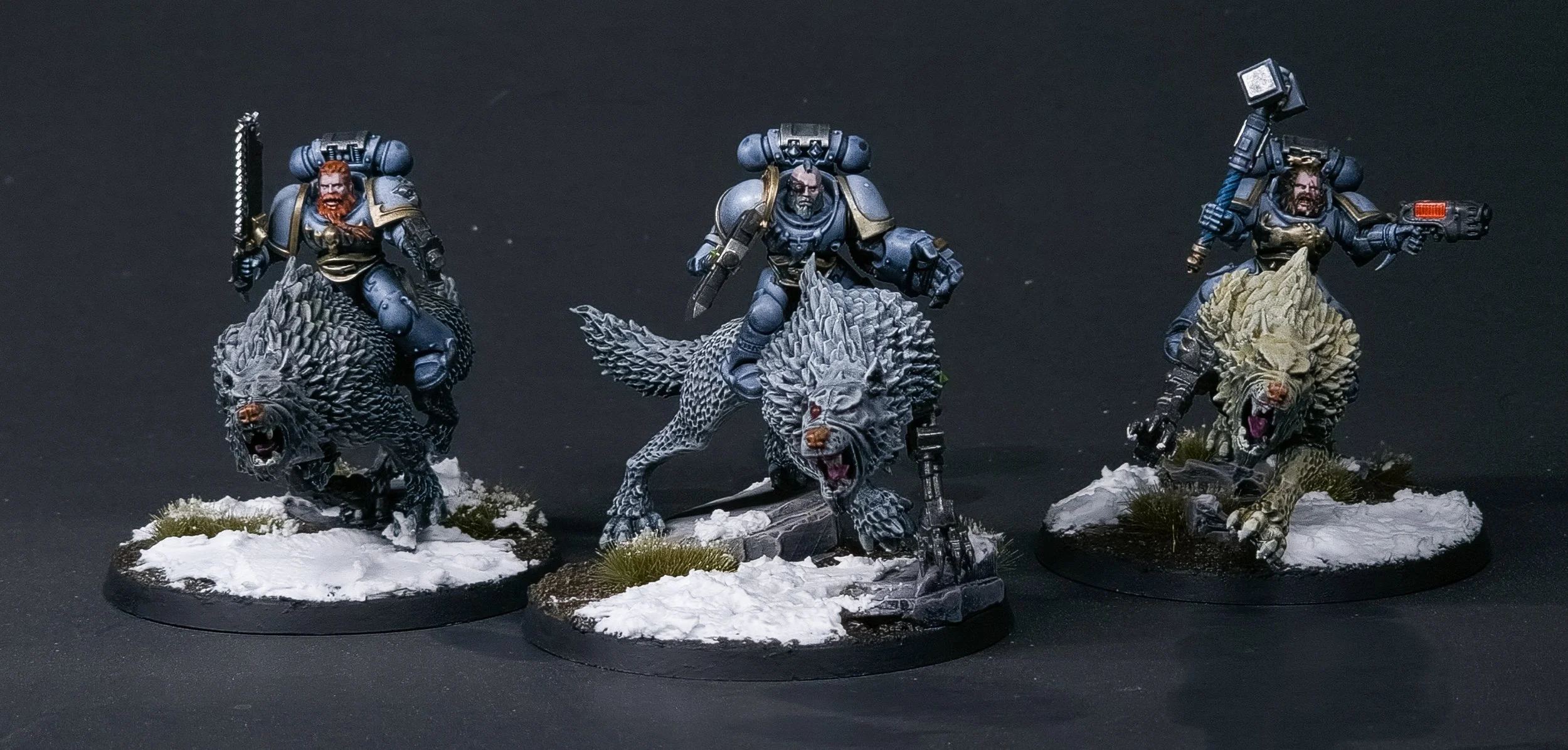 Three miniature figurines of armored soldiers riding wolf-like creatures on snowy bases against a black background.