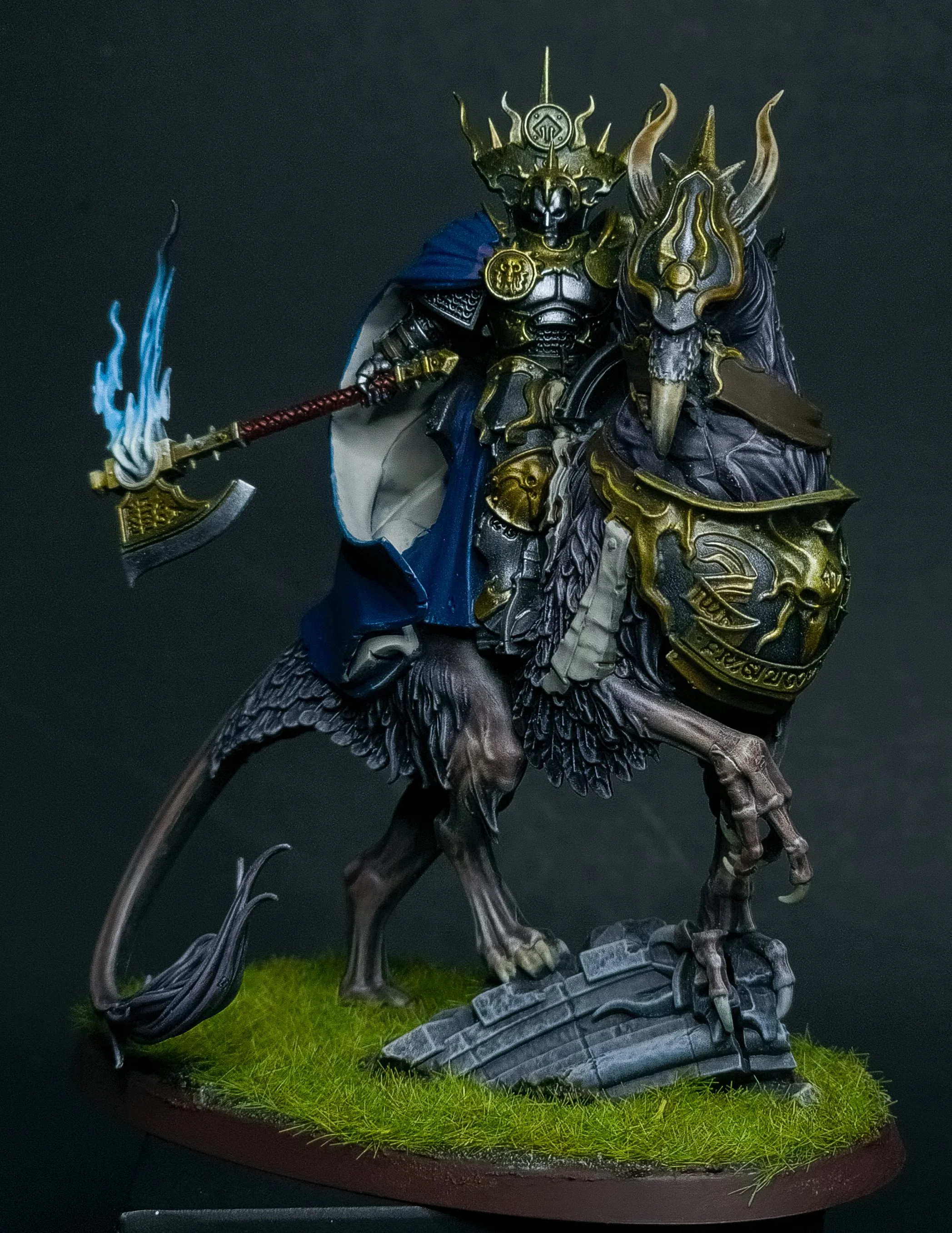 A detailed miniature figure of a fantasy warrior riding a beast, holding a flaming weapon with blue flames, on a grassy base.