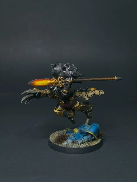 Miniature figurine of a robot with a spear attacking a fallen soldier in blue armor on a round base.