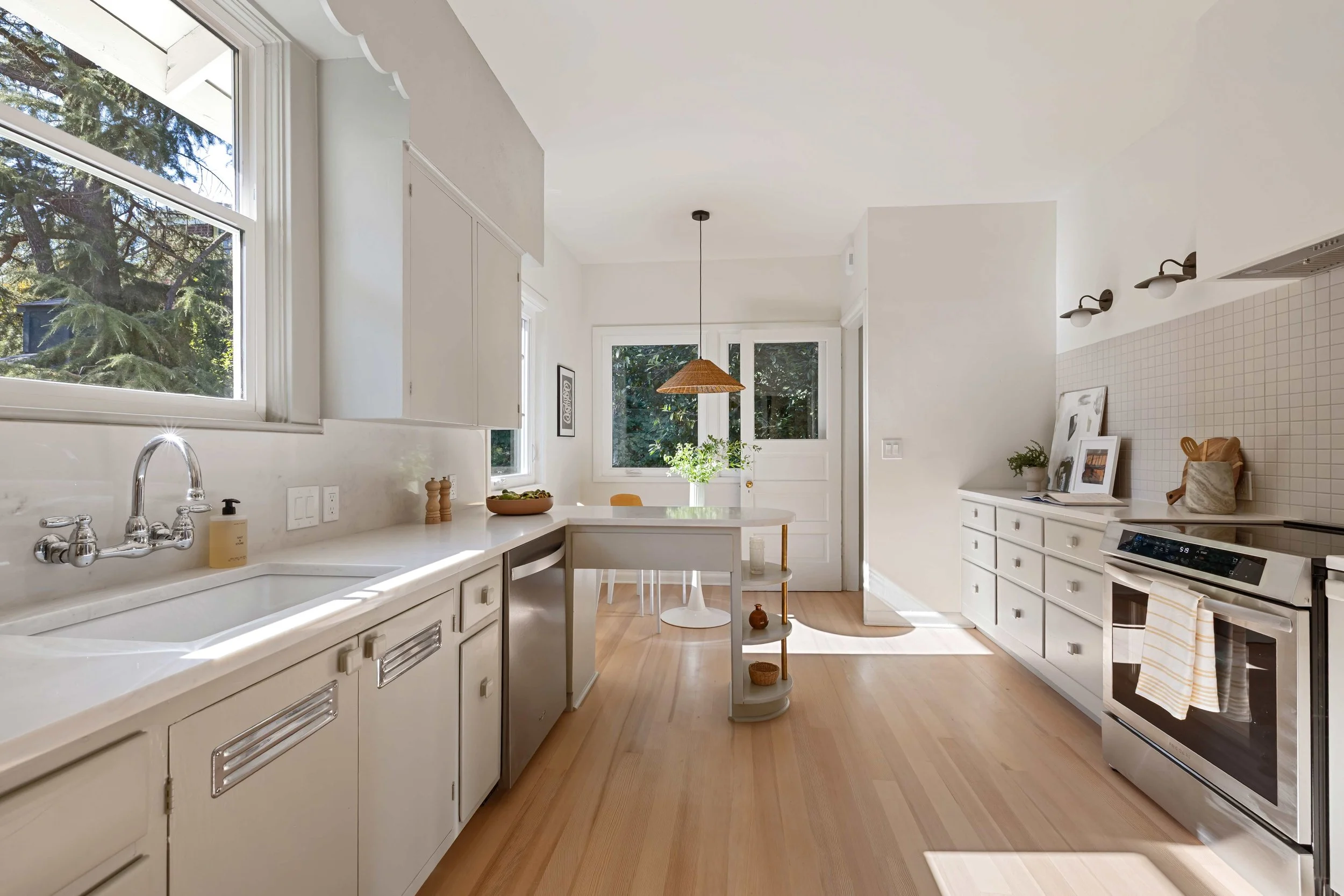 Bright and airy kitchen with white cabinets, hardwood floors, large windows, and modern appliances.