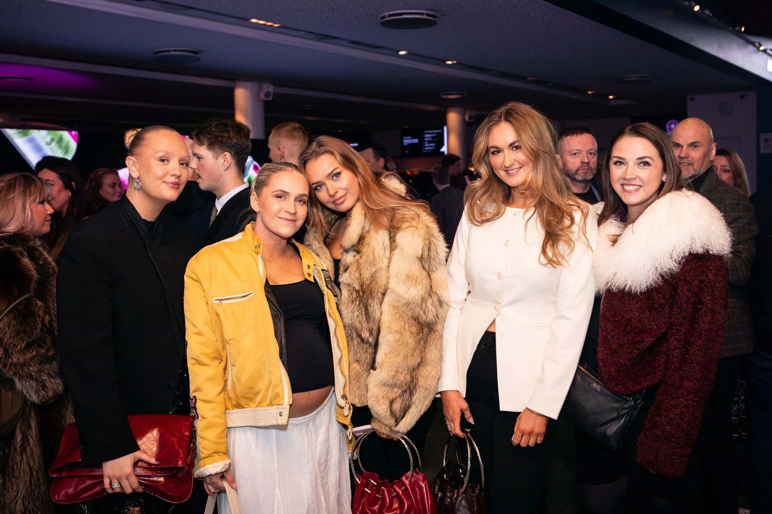 A group of well-dressed people at a social event or party, smiling and posing for a photo indoors.