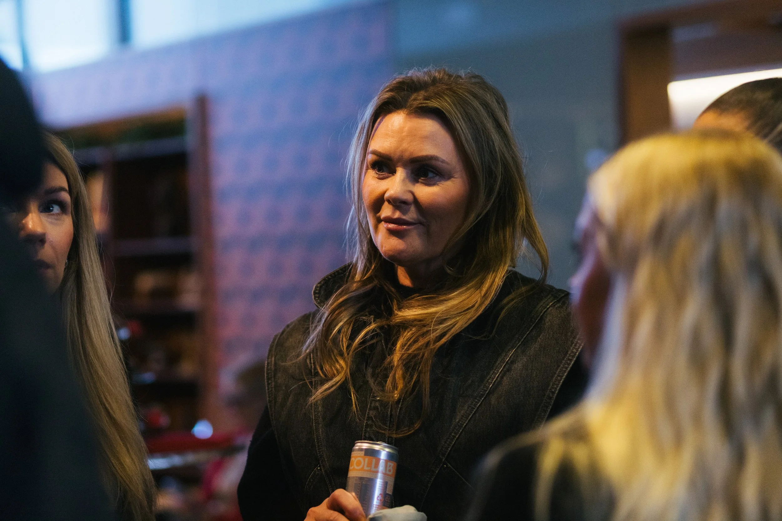 A woman with long brown hair talking to two other women in a dimly lit indoor setting.