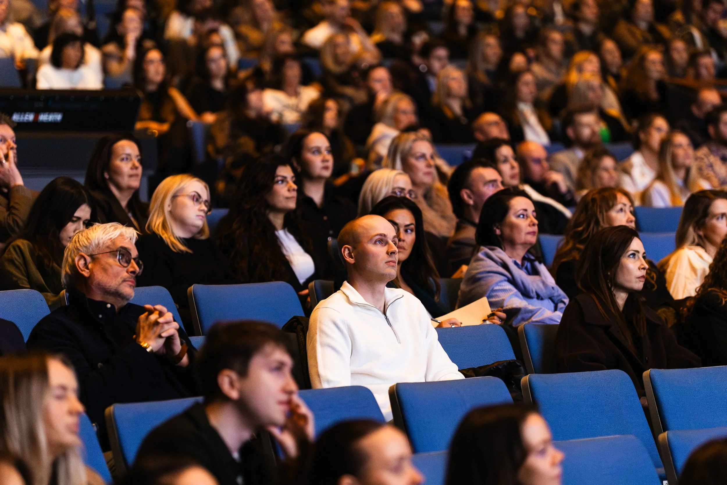 Audience members attentively listening at a conference or seminar in a large auditorium.