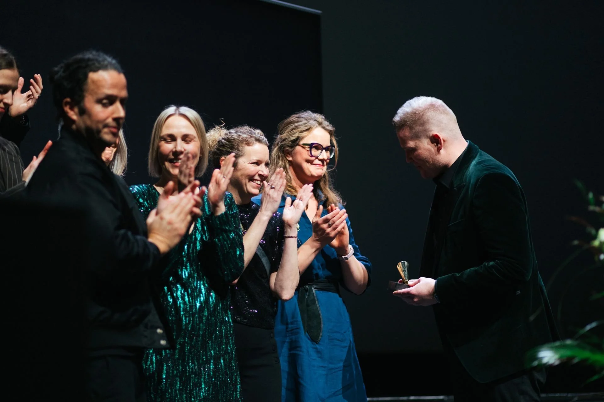 People on stage during an award ceremony, with one person receiving a trophy as others applaud.