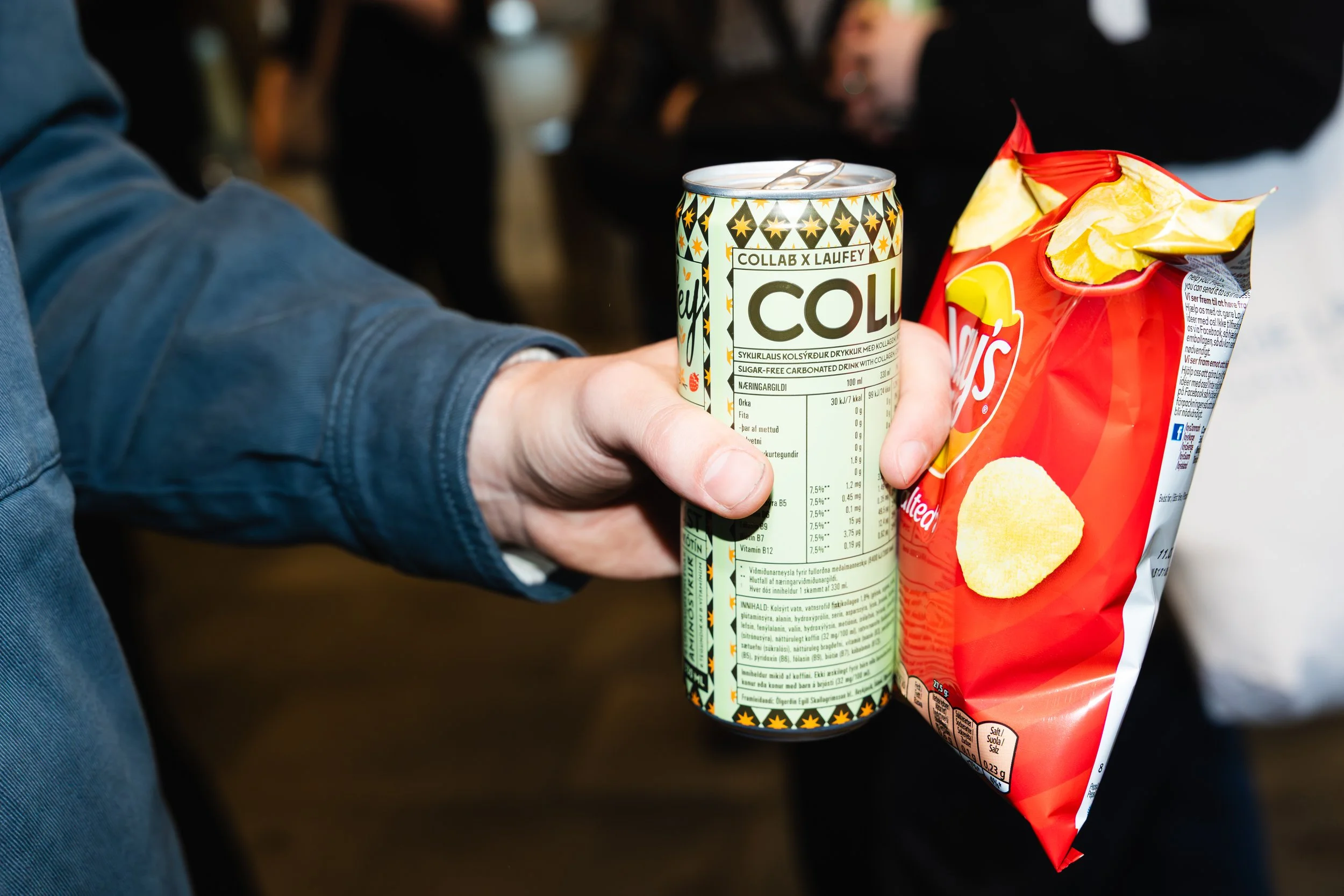 A person's hand holding a can of sugar-free cola next to a bag of potato chips.