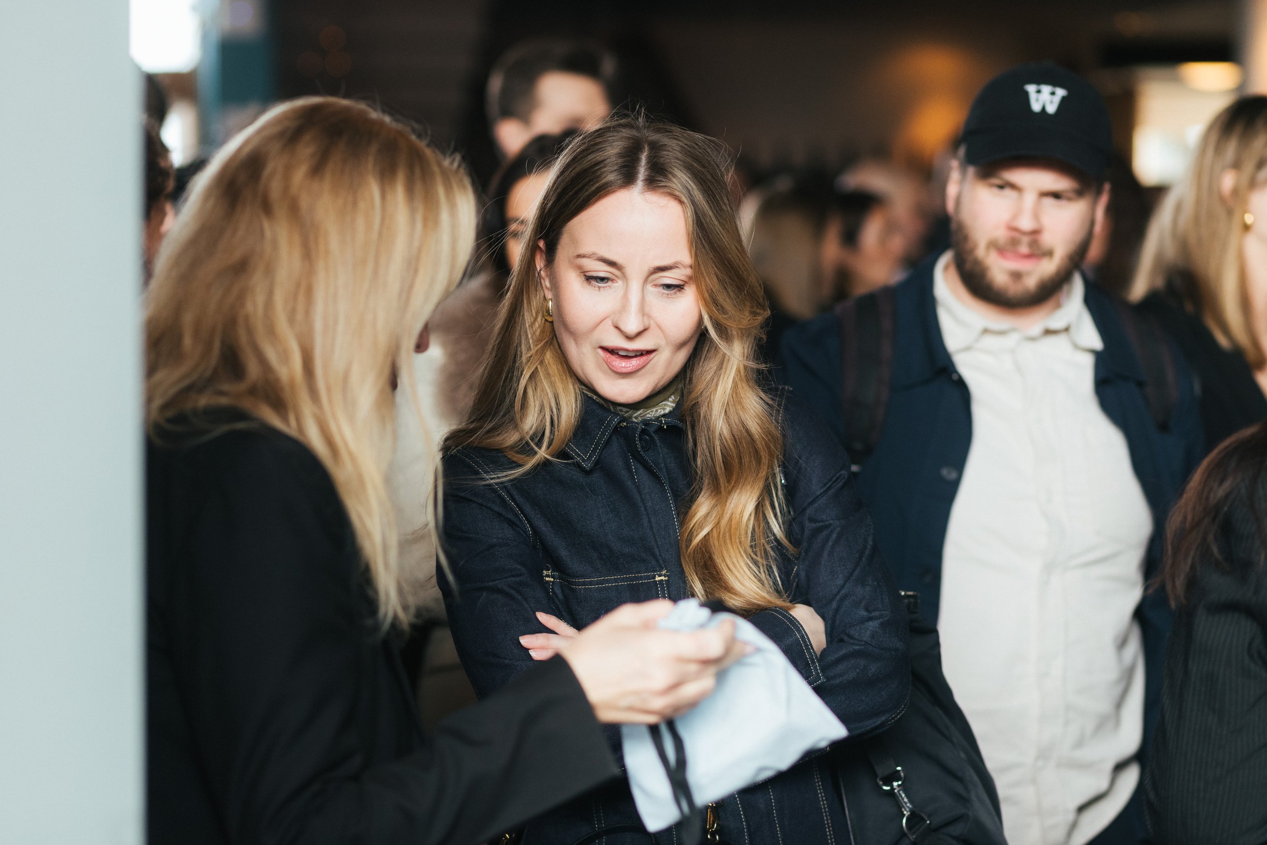 A group of young adults standing and conversing in a busy indoor setting, possibly a social event or gathering.