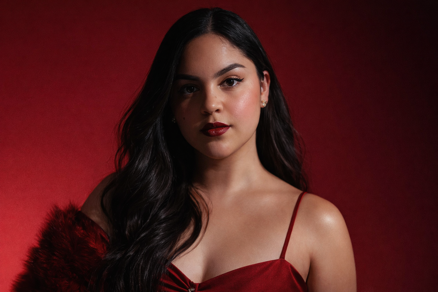 Ale Abella. Alejandra Abella. Ale Abella Nails . Retrato de una mujer joven con cabello largo y oscuro, usando un vestido rojo con tirantes y un abrigo de felpa rojo, en fondo rojo.