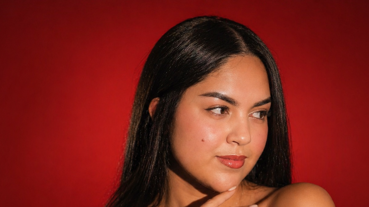 Retrato de una mujer con cabello largo y oscuro, piel clara y labios rojizos, en un fondo rojo.