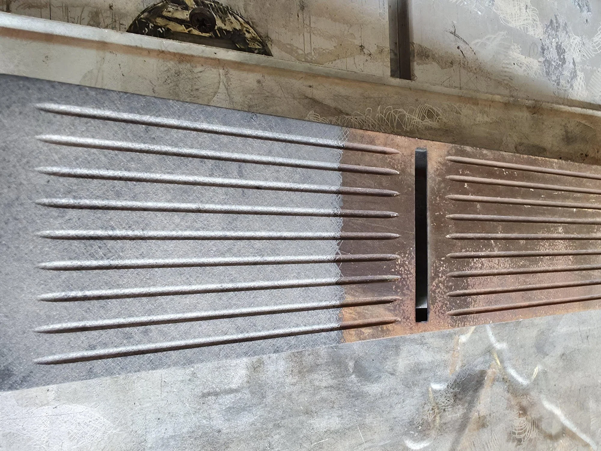 Close-up of metal grate or vent with parallel bars, placed on a concrete or stone surface.